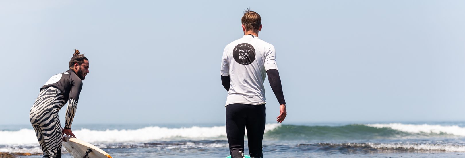 Waterbound instructor and student walking into the sea for a surf lesson in Ericeira